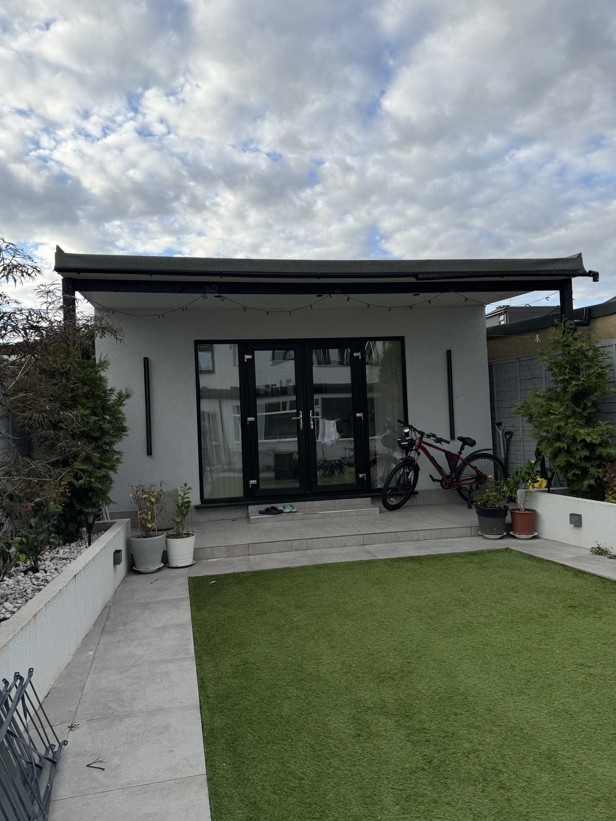 The garden tuition studio in Barking, with glass doors opening onto a paved terrace and lawn